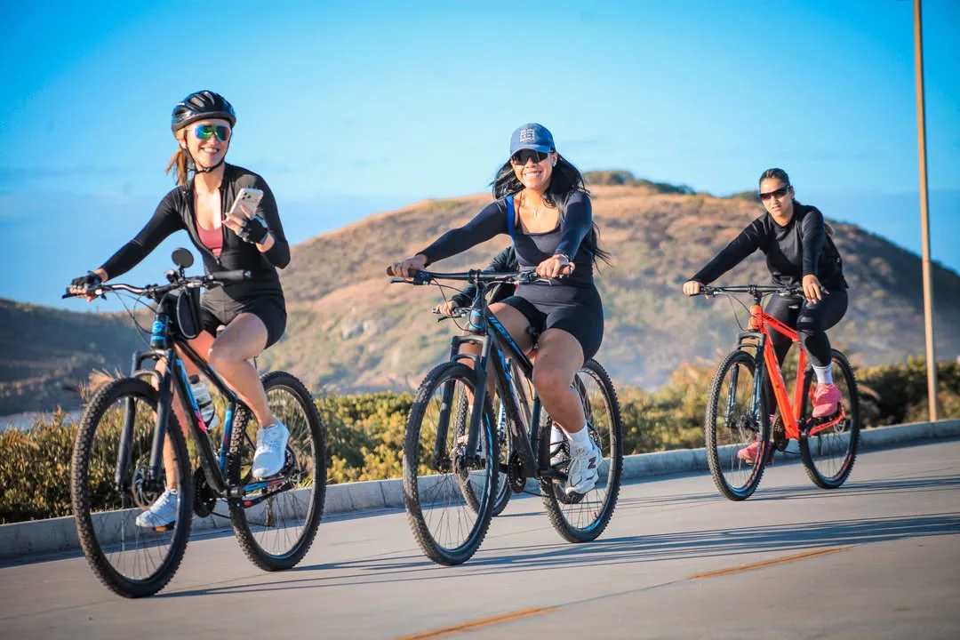 Três ciclistas pedalando em estrada com um morro ao fundo