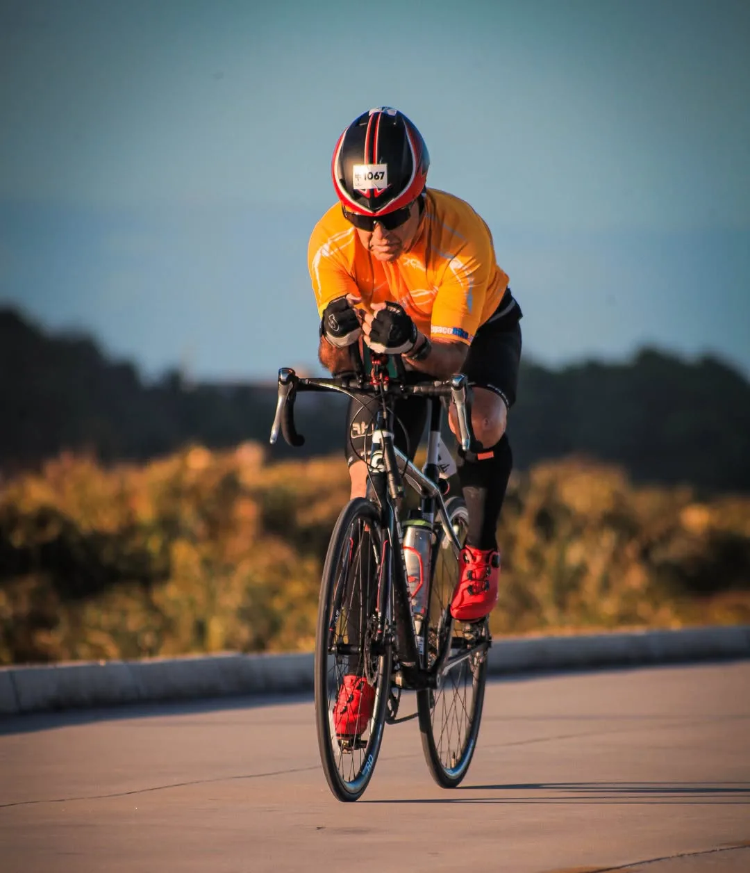 Ciclista de camisa laranja pedalando em direção à câmera