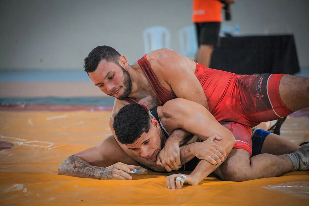 Lutador de vermelho dominando o adversário no tatame laranja