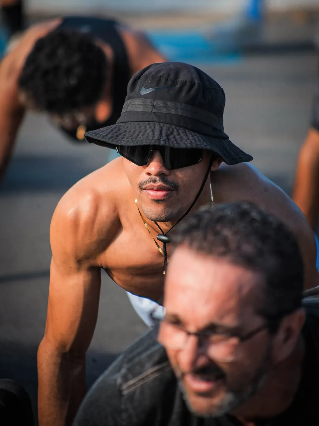 Participante de chapéu e óculos escuros agachado no asfalto