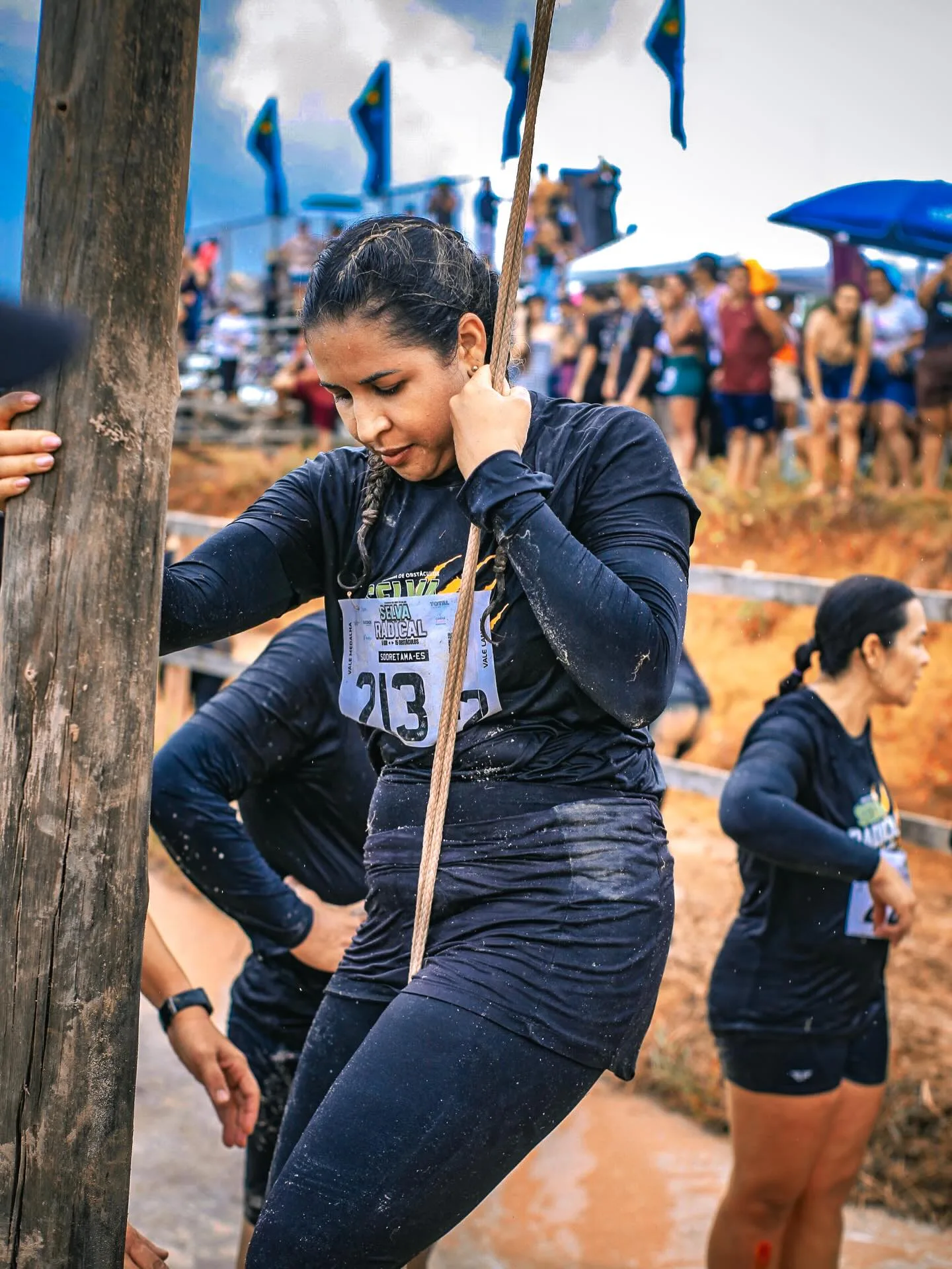 Participante puxando uma corda na lama, com público ao fundo