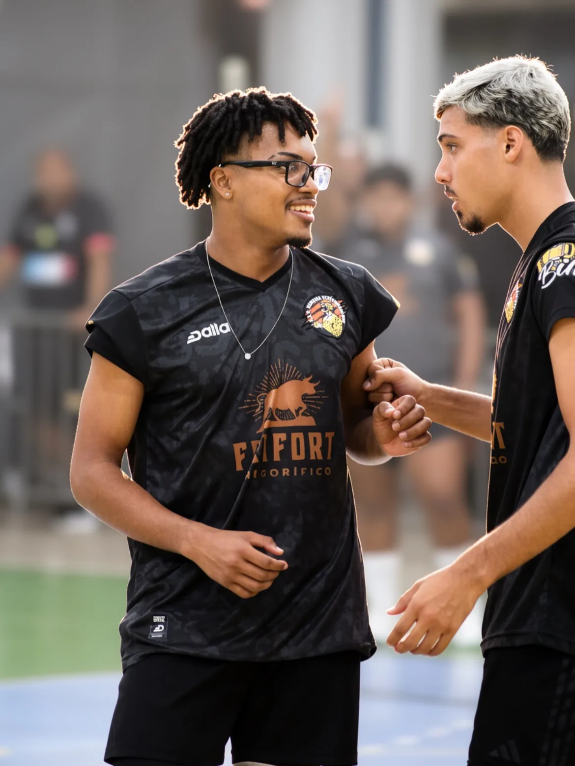 Dois atletas de camiseta preta conversando no ginásio