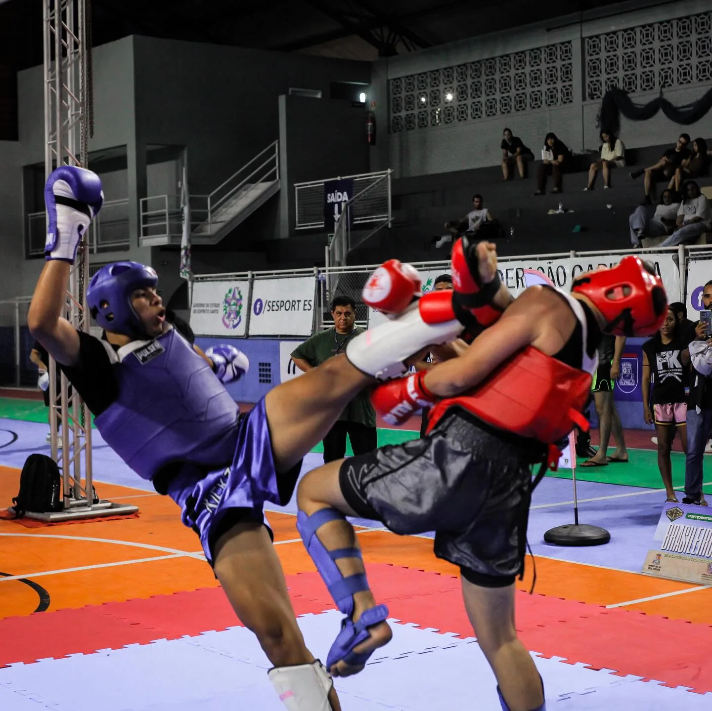 Lutador de capacete roxo aplicando um chute alto no adversário