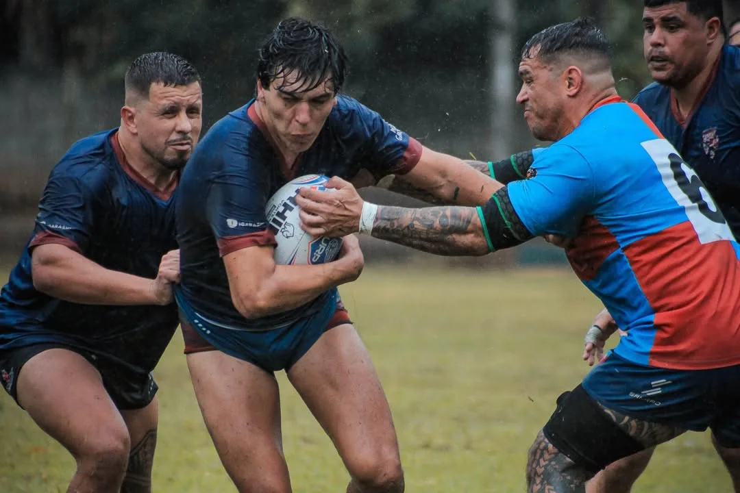 Jogador de rugby carregando a bola entre dois adversários